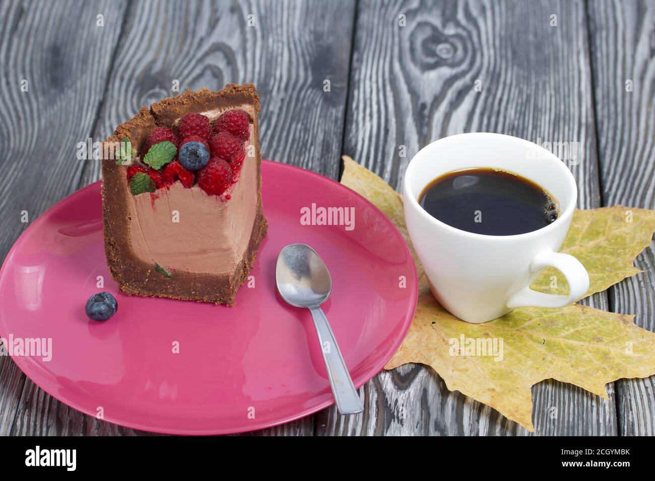 Un pezzo di torta al cioccolato senza forno con formaggio cremoso. Guarnito con lamponi, mirtilli e foglie di menta. Nelle vicinanze si trova una tazza di caffè e di mapl secco Foto Stock