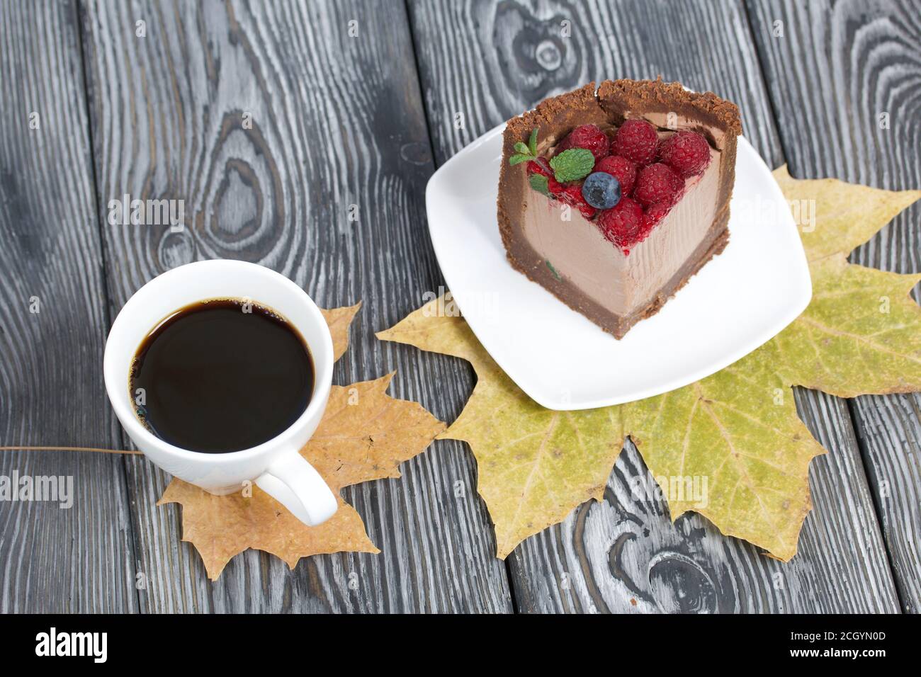 Un pezzo di torta al cioccolato senza forno con formaggio cremoso. Guarnito con lamponi, mirtilli e foglie di menta. Nelle vicinanze si trova una tazza di caffè e di mapl secco Foto Stock