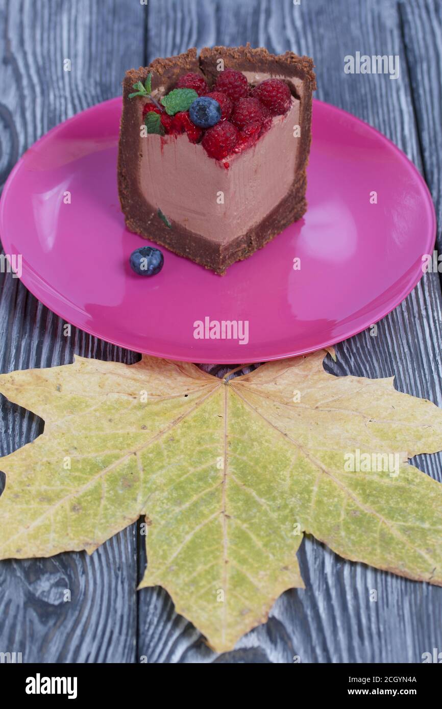 Un pezzo di torta al cioccolato senza forno con formaggio cremoso. Guarnito con lamponi, mirtilli e foglie di menta. Nelle vicinanze si trova una foglia di acero secca. Sul sur Foto Stock