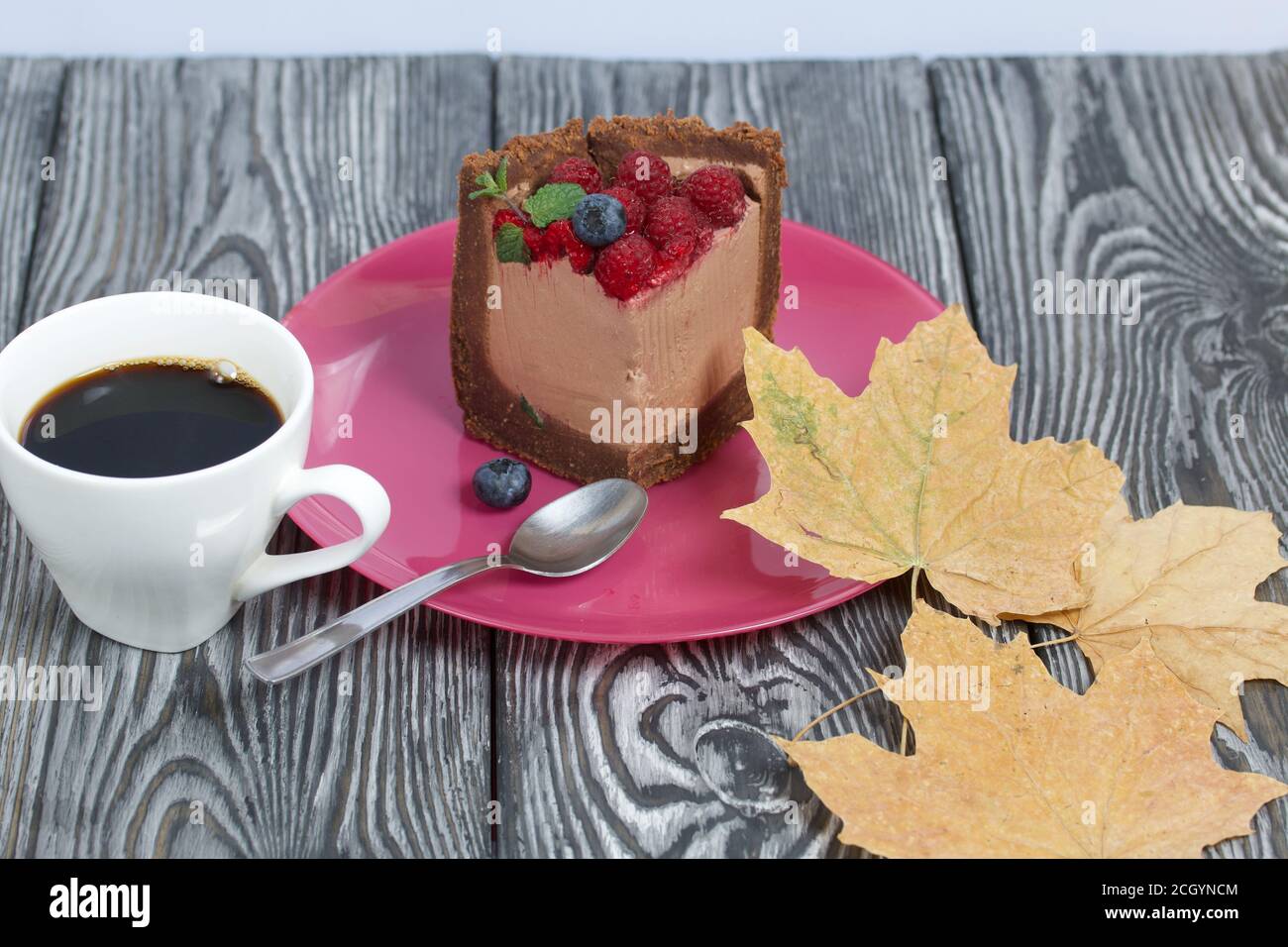 Un pezzo di torta al cioccolato senza forno con formaggio cremoso. Guarnito con lamponi, mirtilli e foglie di menta. Nelle vicinanze si trova una tazza di caffè e di mapl secco Foto Stock