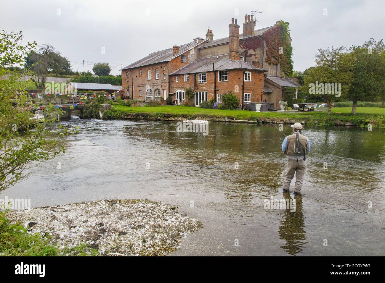 Un pescatore pesca di fronte a una bella vecchia casa mulino sul fiume Kennet a Hungerford, Berkshire Foto Stock