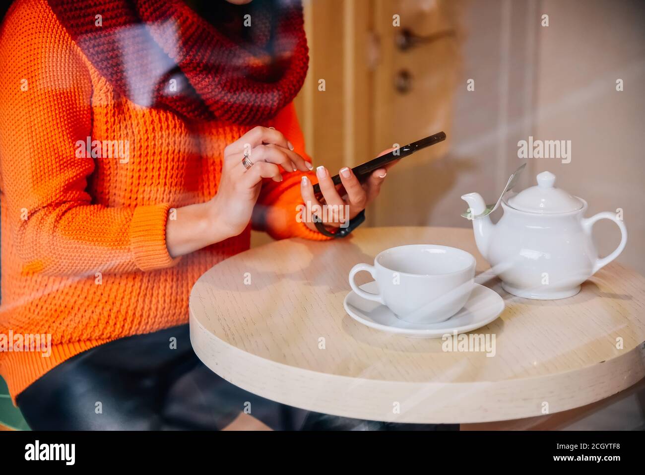 Ragazza al caffè con telefono. La ragazza sta guardando un feed di notizie in un caffè con una tazza di tè. Visualizza attraverso la finestra. Foto Stock