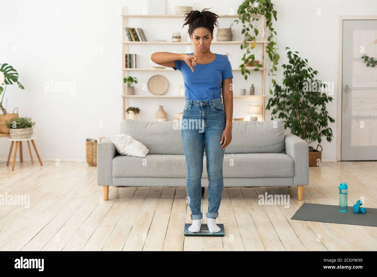 Frustrata Black Girl gesturing Thumbs-down in piedi su scale in interni Foto Stock