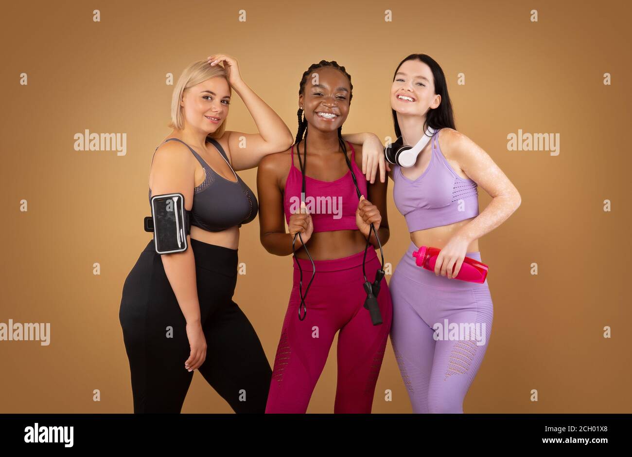 Sorridi donne multirazziali con diverso tipo di figura in sportswear over sfondo marrone Foto Stock