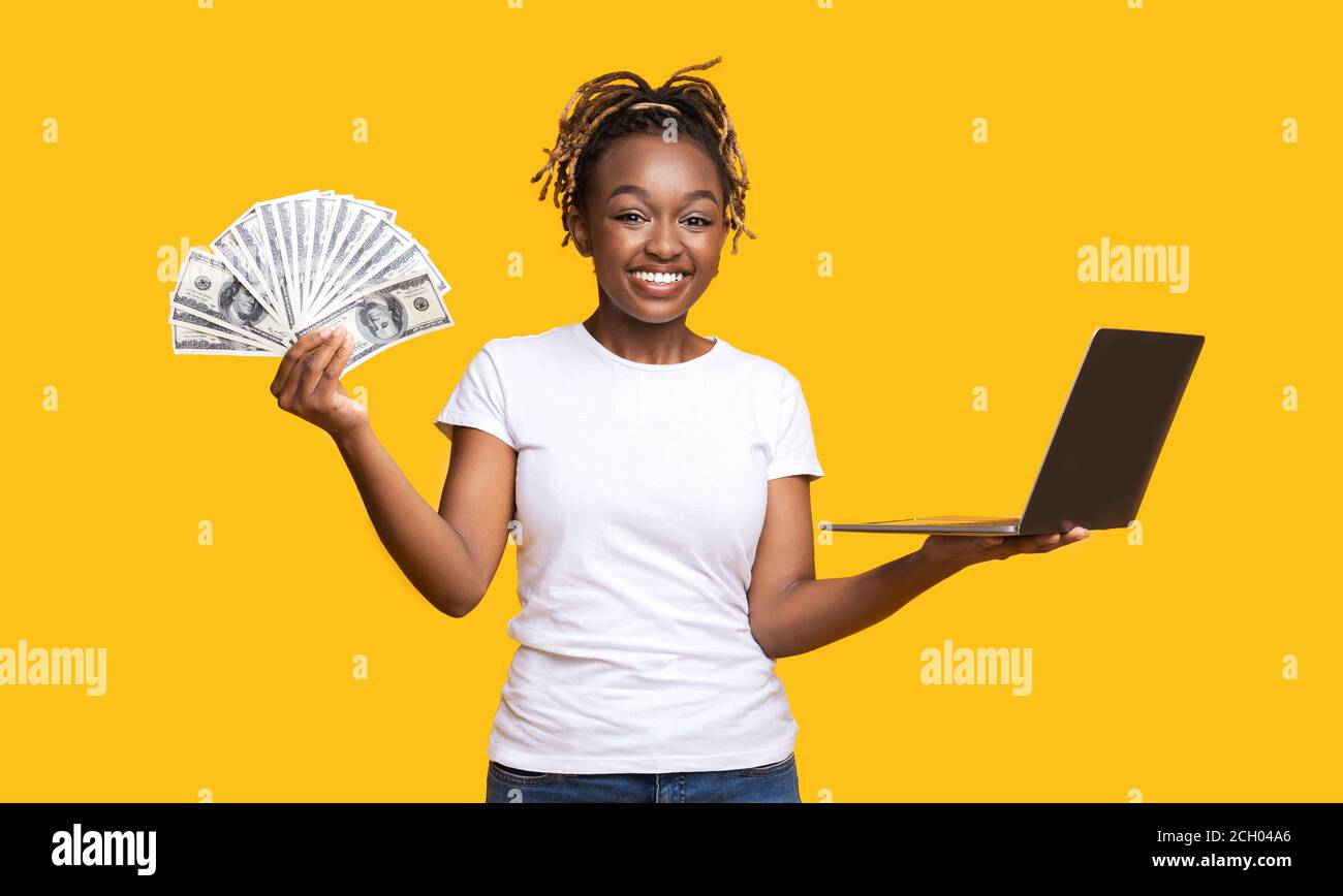 Gioiosa ragazza nera con contanti e laptop in giallo Foto Stock