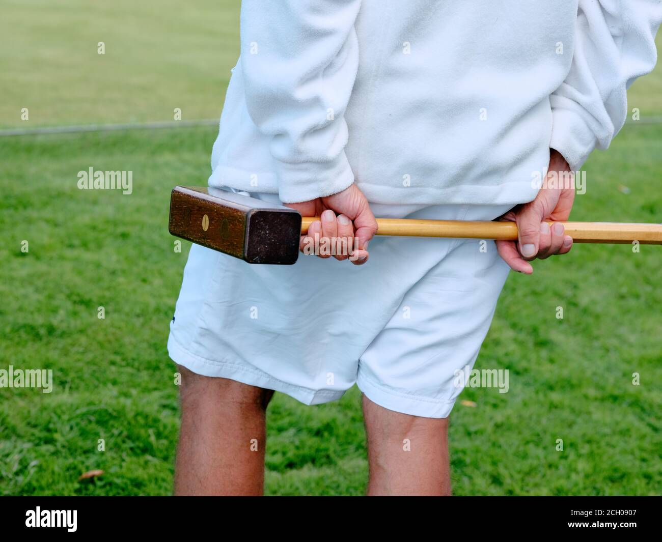 Un uomo vestito in bianco tradizionale che gioca il croquet del prato e tiene un mazzuolo del croquet. Foto Stock