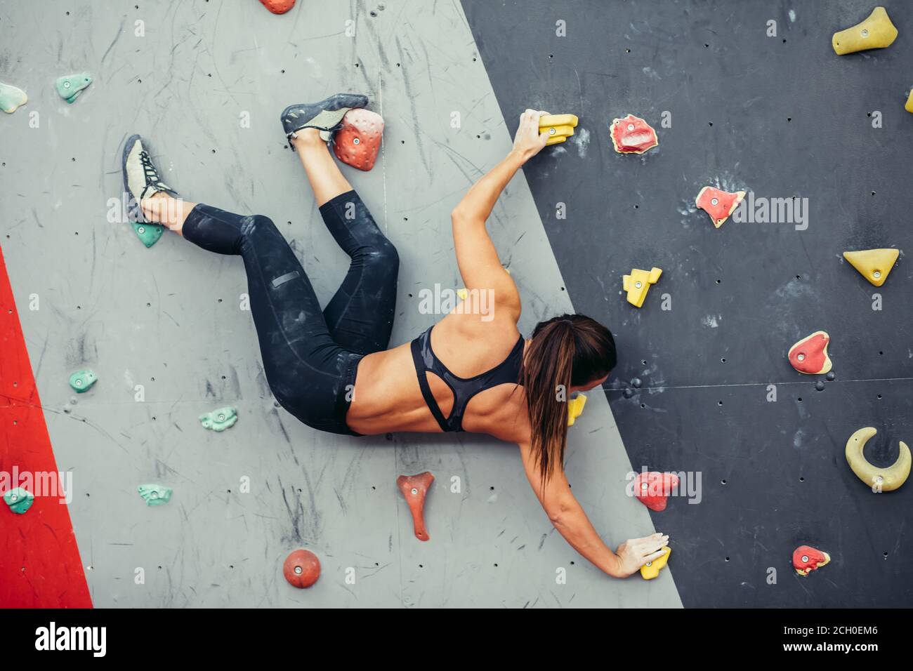 vista posteriore della sportiva muscolare che scende da una parete artificiale al centro dell'arrampicatore senza imbracatura o fune di sicurezza. Foto Stock