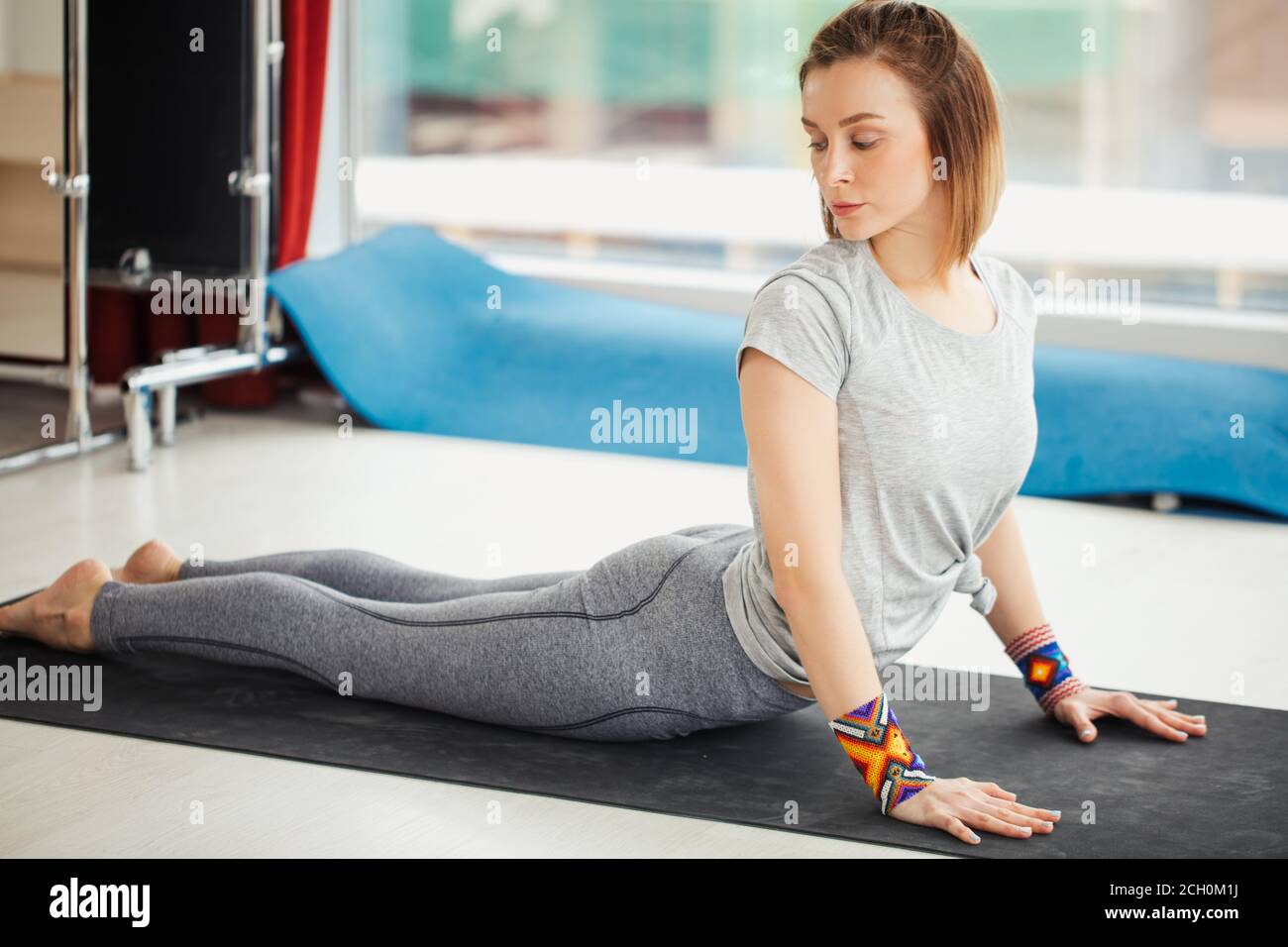 Yoga donna fare esercizio stretching su tappetino in studio ben illuminato sfondo. Foto Stock