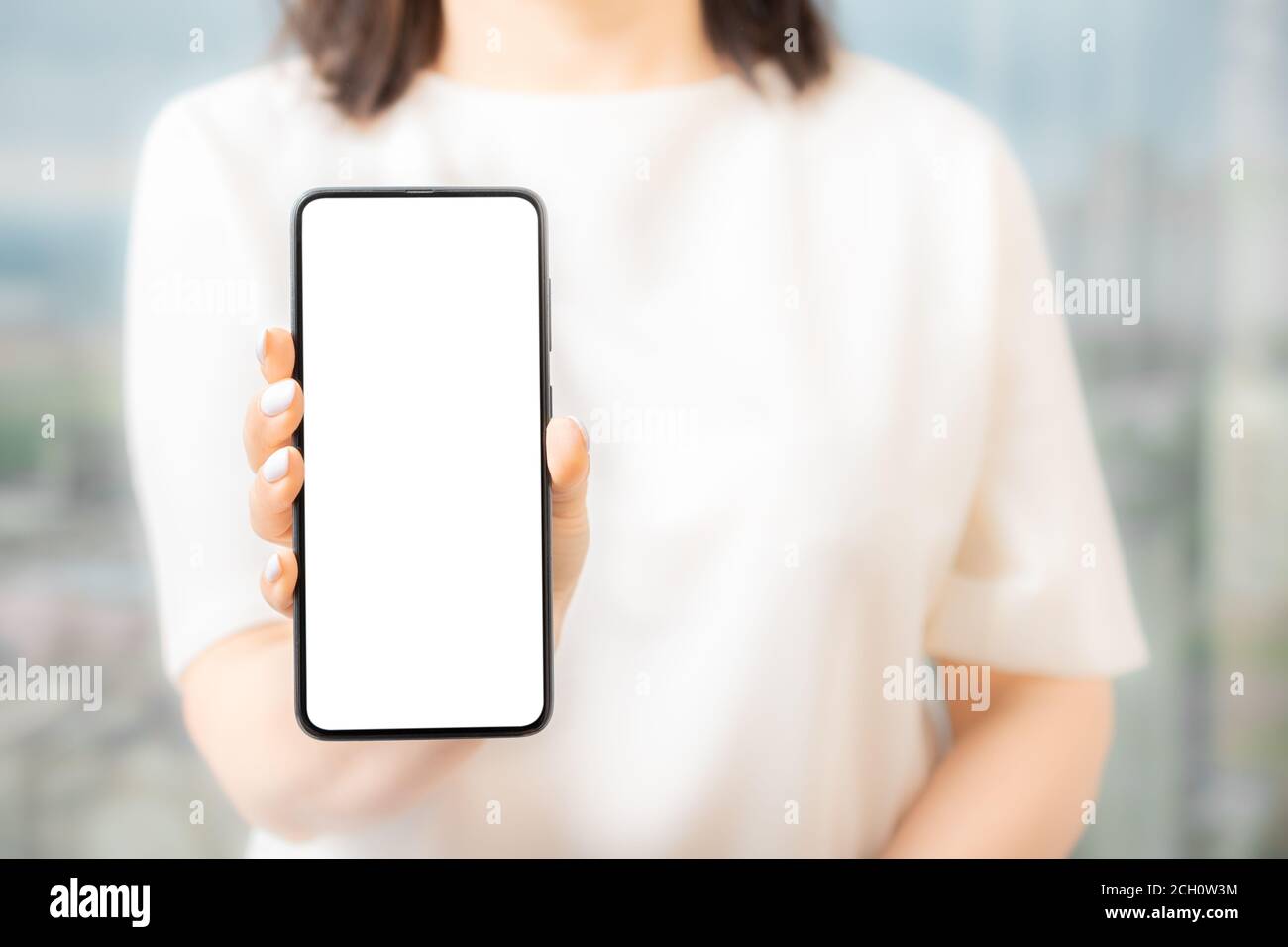 Donna in abito bianco che mostra schermo vuoto cellulare Donne mano mostra il telefono cellulare al bianco schermo, mockup Foto Stock