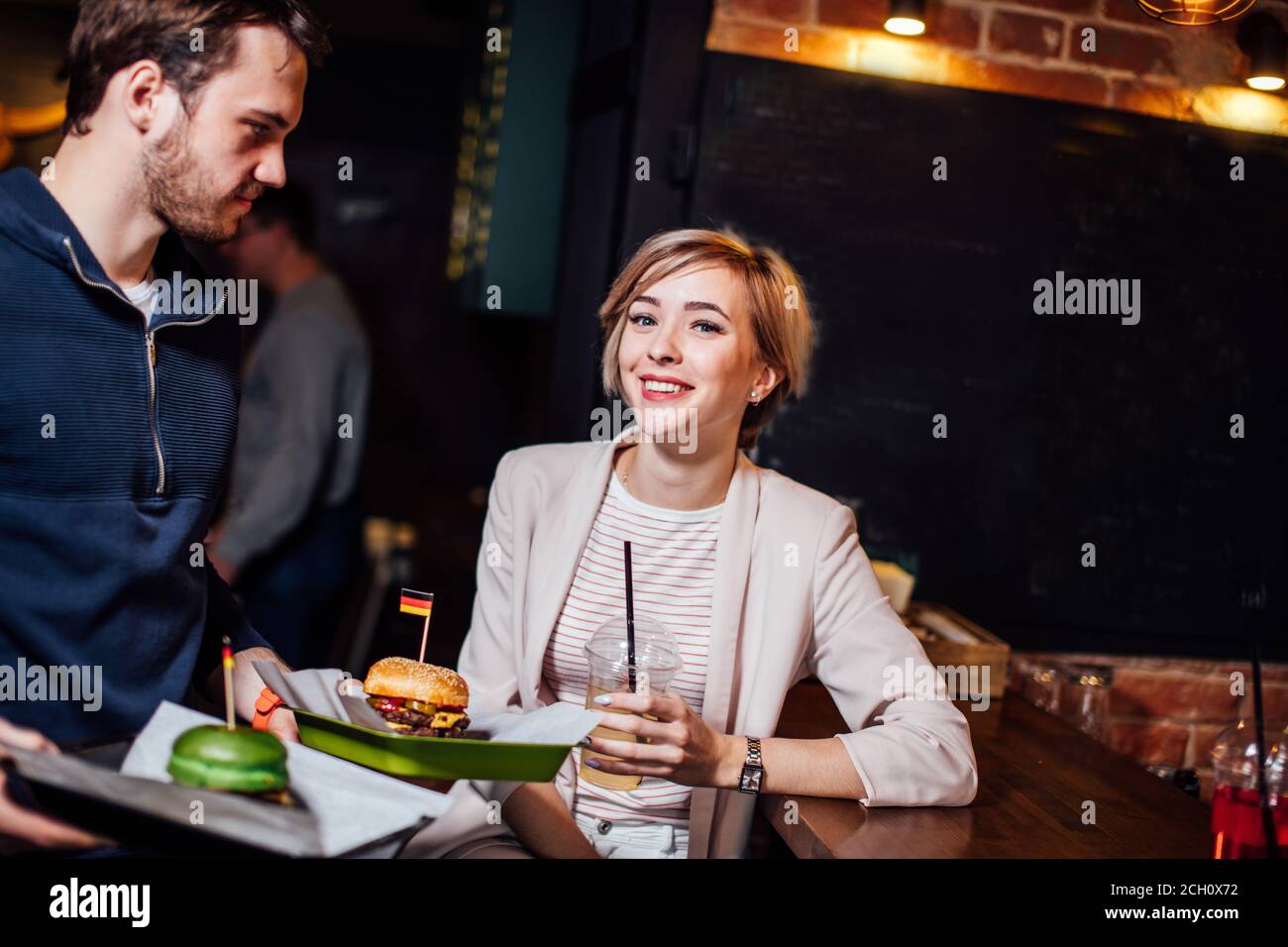 Bella donna che guarda la macchina fotografica in attesa di cameriere per portare il suo ordine in ristorante. Foto Stock