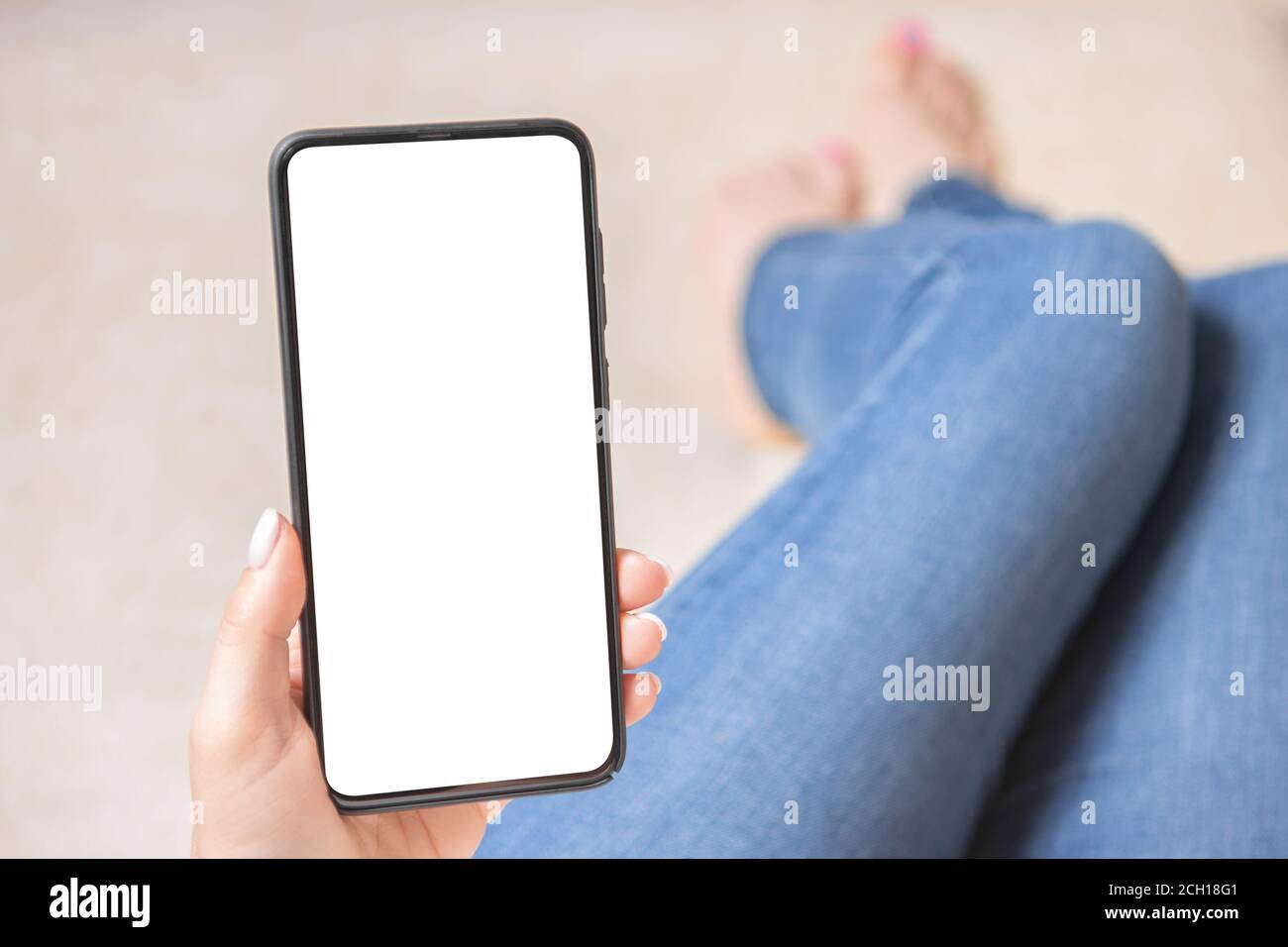 Immagine mockup delle mani di donna che tengono il telefono cellulare con schermo vuoto. Donna è seduta sul divano con le gambe allungate. Mockup cellulare pho Foto Stock