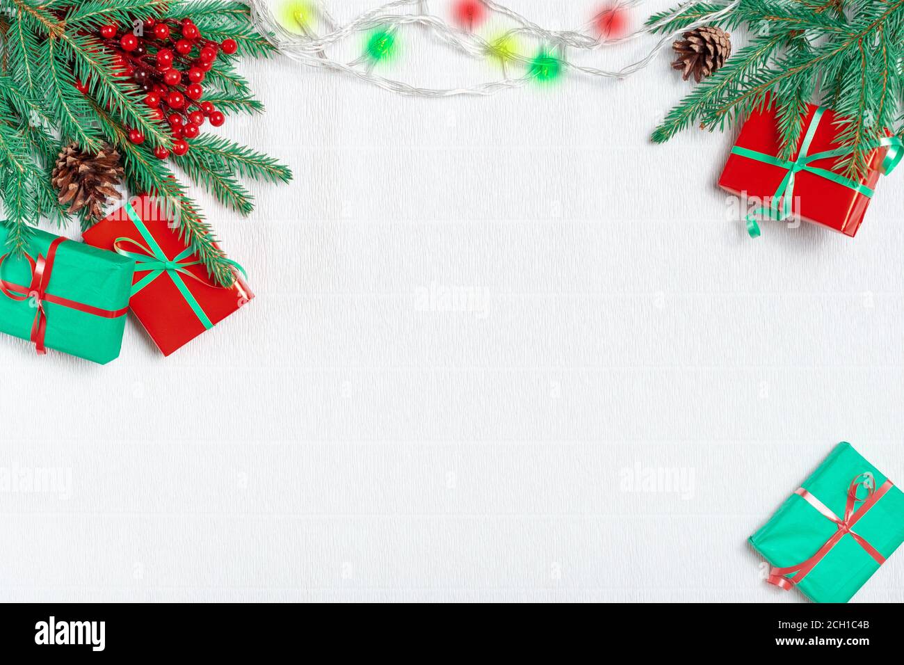 Bella cornice di Natale di rami di abete, scatole regalo, rosso agrifoglio decorato da luci di natale. Vista dall'alto Foto Stock