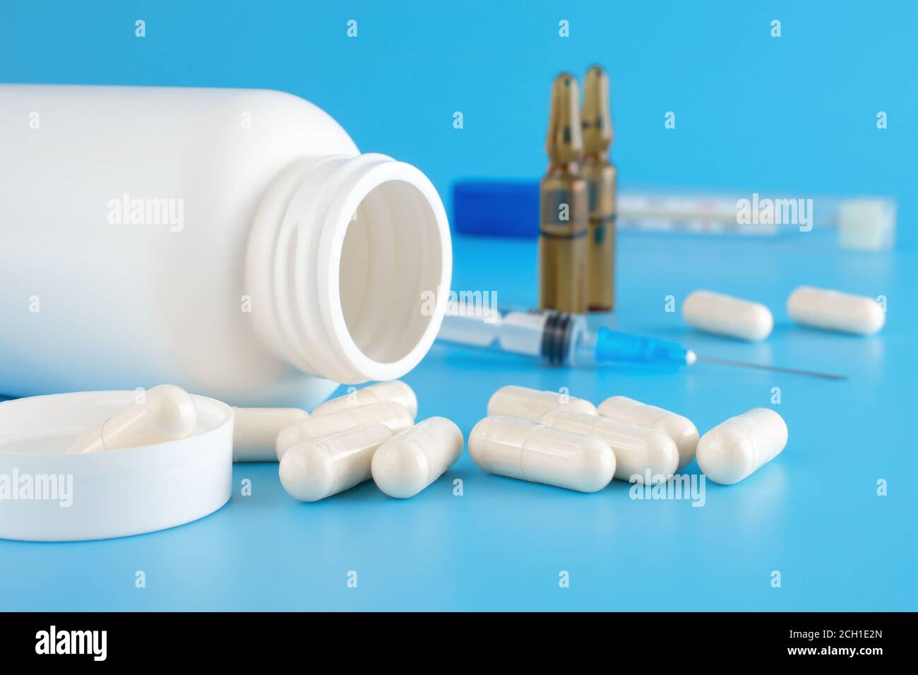 Le pillole fuoriescono dal contenitore bianco. Contenitori medici, pillole, siringhe, fiale per preparazioni iniettabili su sfondo medico blu. Medicinali diversi Foto Stock