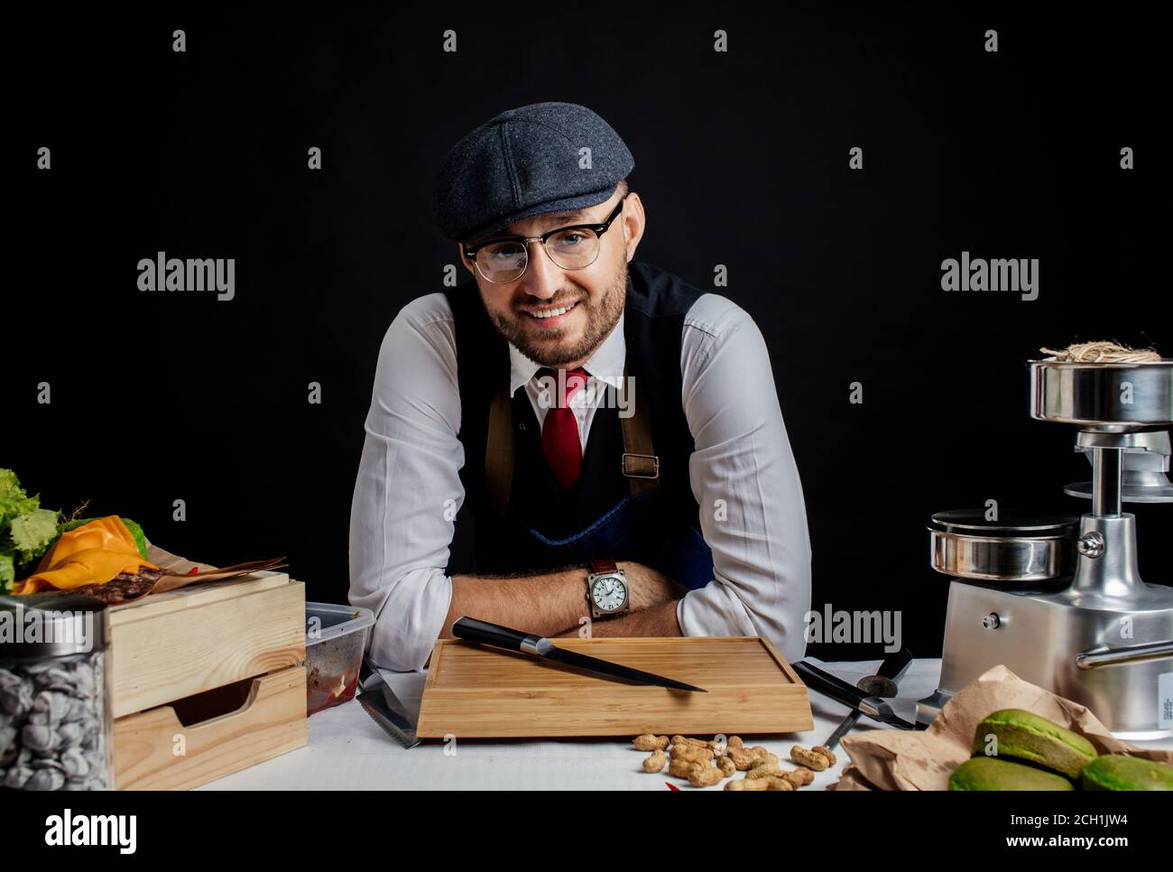 concetto di piccola impresa, cibo e gente - elegante barman felice al tavolo con utensili da cucina all'hamburger cafe o caffetteria. Foto Stock
