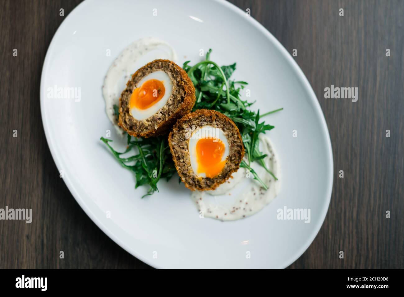 Scotch Egg Cut a metà con Golden yolk servito Un piatto e insalata di razzi Foto Stock