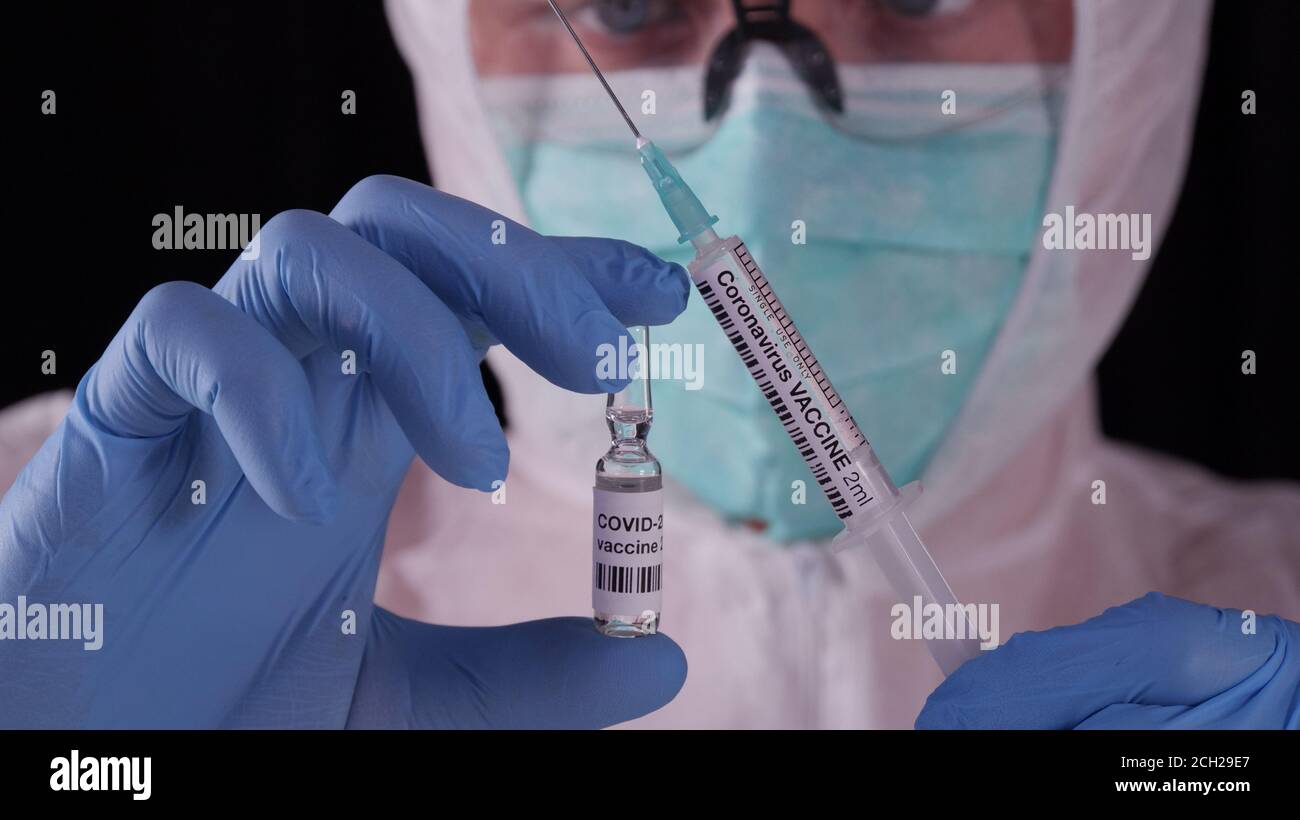 Vaccino del coronavirus. Uomo in uniforme bianca di sicurezza, maschera e occhiali contenenti fiala e siringa di vaccino del coronavirus. COVID-19 concetto di cura pandemica Foto Stock