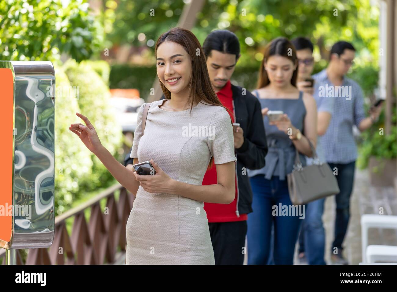 Donna asiatica che usa un chiosco di ordinazione di cibo con coda a distanza sociale in coda prima di entrare in fast food ristorante. Tecnologia online self-service novità Foto Stock