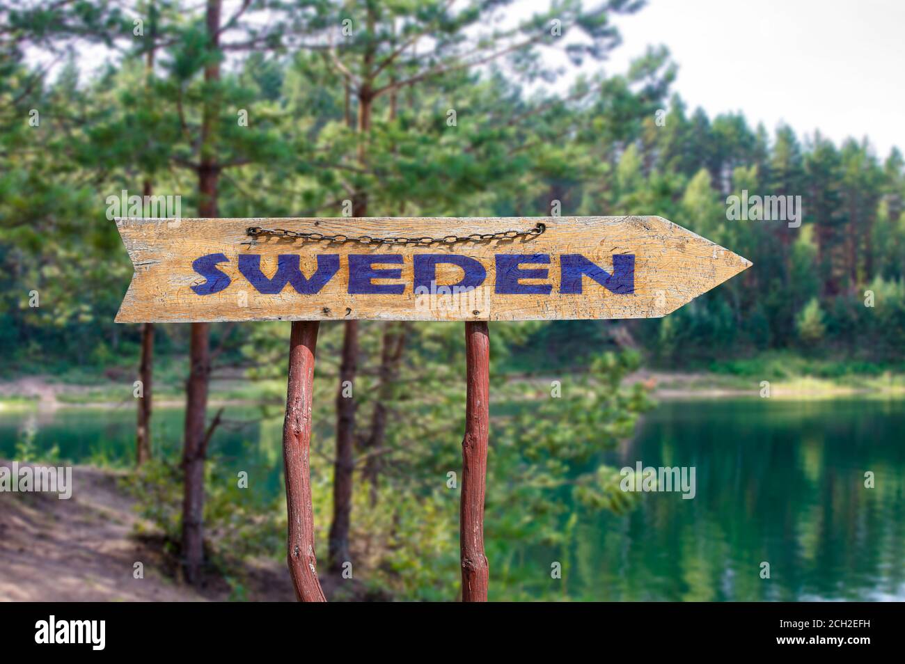 Svezia freccia in legno segno strada contro il lago e pini sfondo. Viaggio in Svezia Concept. Foto Stock