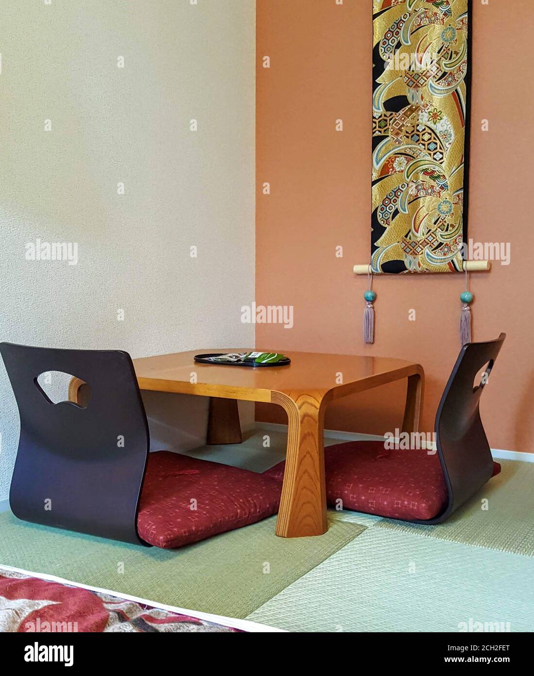 Piccola area da pranzo giapponese con tavolo, posti a sedere e arte murale su un tappeto tatami. Foto Stock