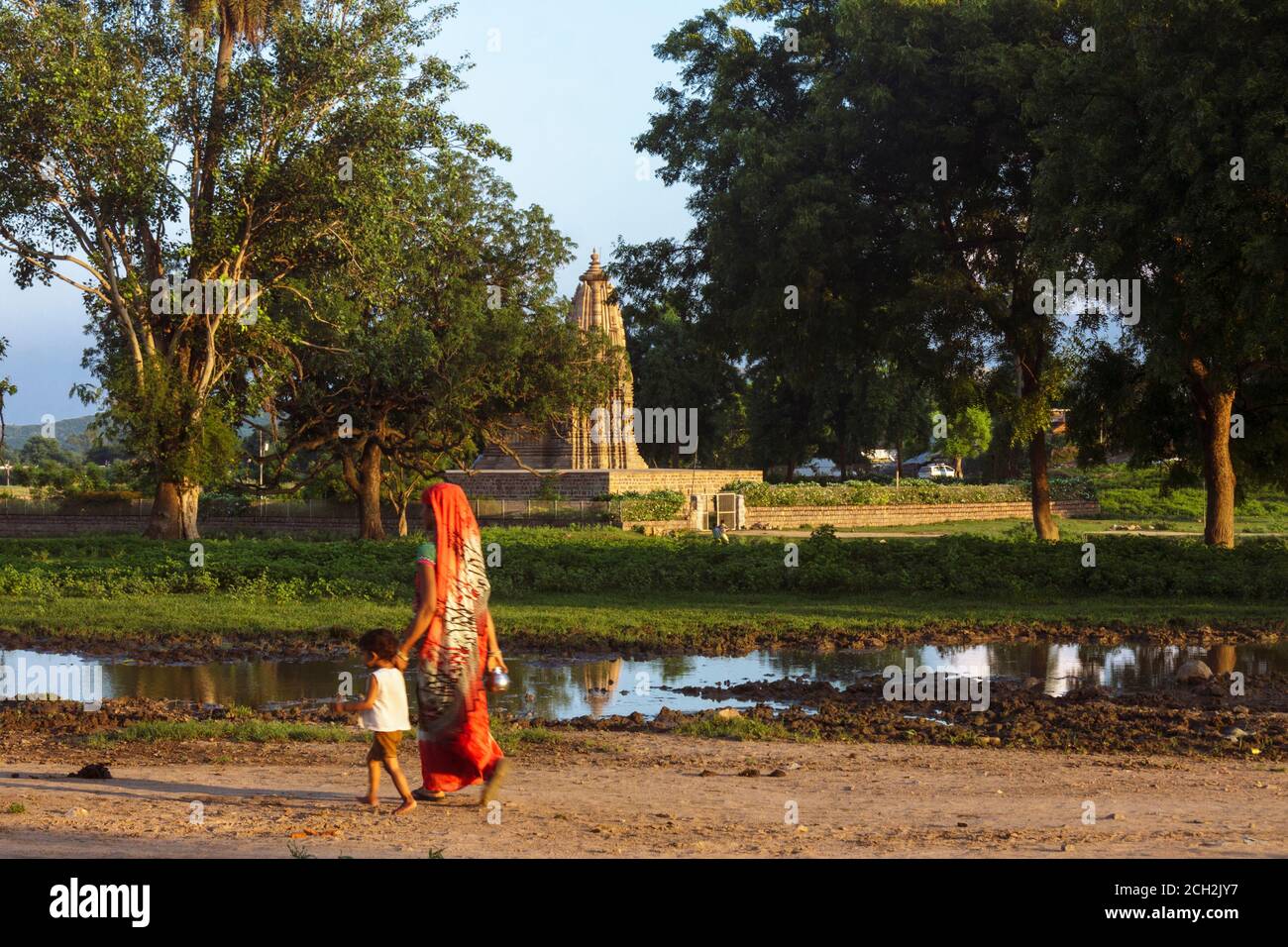 Khajuraho, Madhya Pradesh, India : una donna indiana e un bambino camminano oltre il Tempio Javari, parte del gruppo orientale del sito patrimonio mondiale dell'UNESCO Foto Stock
