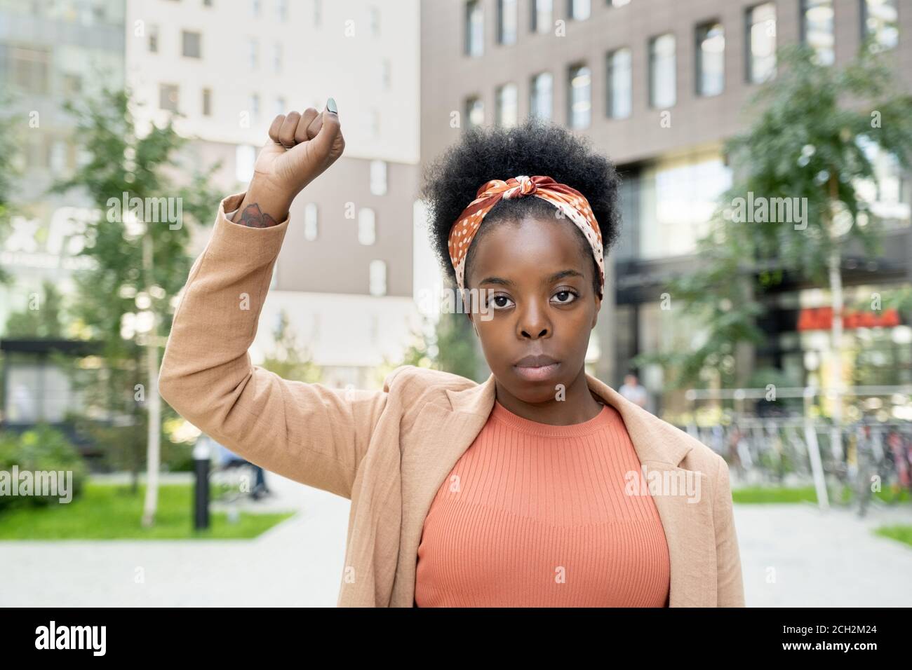 Giovane donna d'affari contemporanea di etnia africana che tiene il braccio destro sollevato Foto Stock