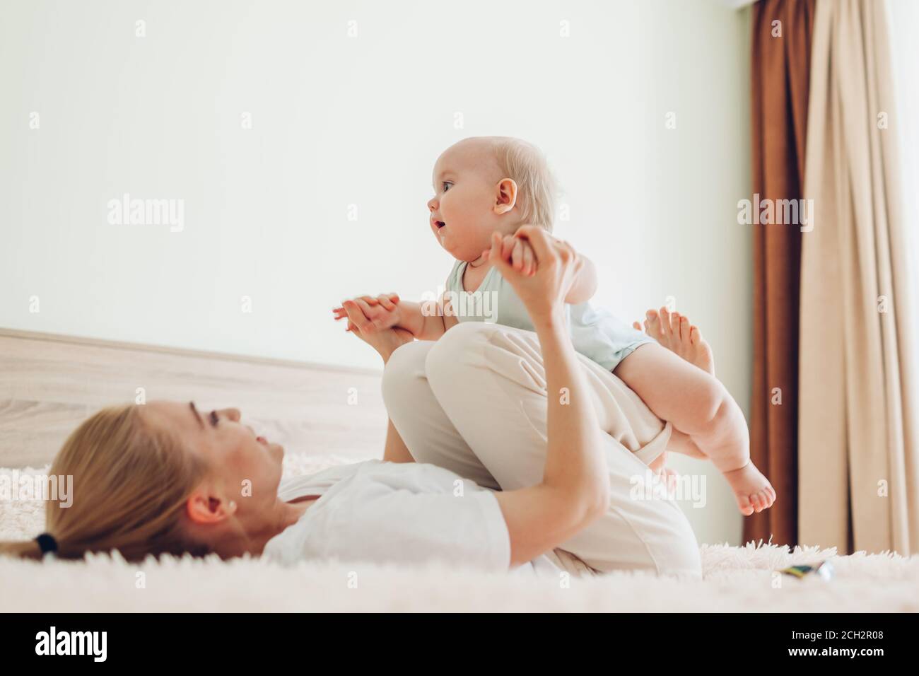 Giovane madre che gioca con il suo neonato figlio a casa. Famiglia che si divertono sdraiati sul letto in camera da letto Foto Stock