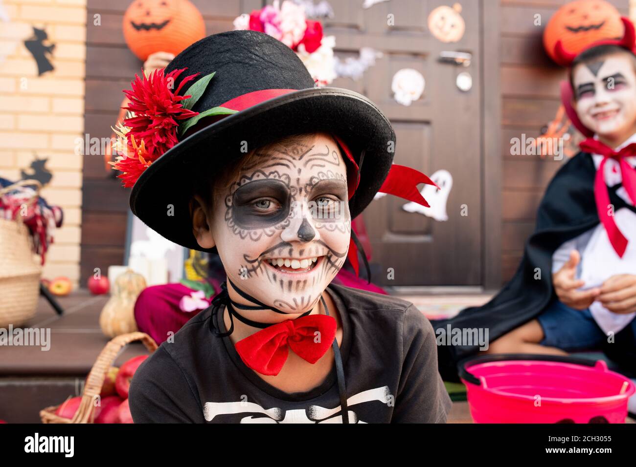 Felice ragazzo carino con la faccia dipinta seduta di fronte fotocamera contro i suoi amici Foto Stock
