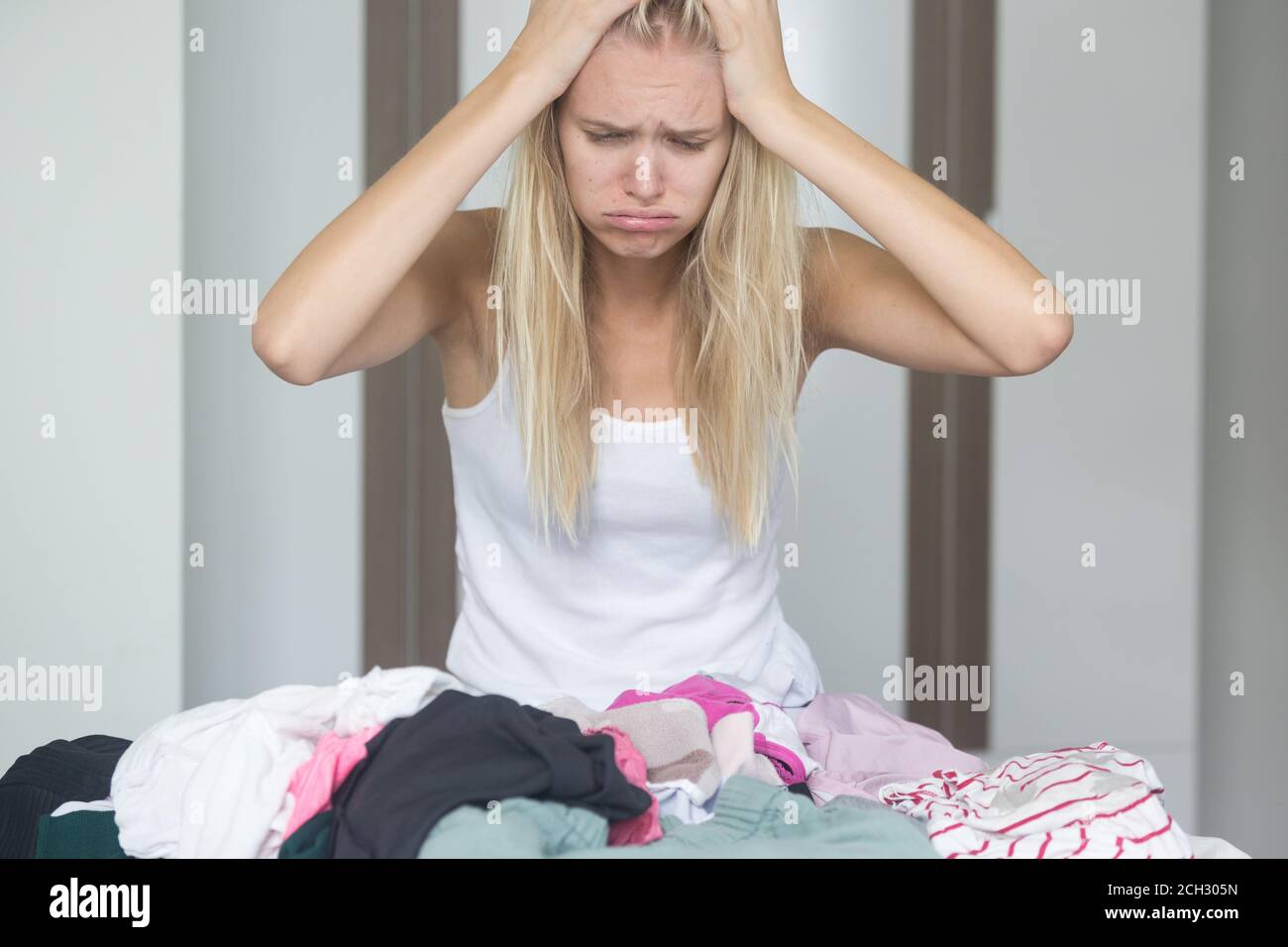 Donna stanca e frustrata che smista i vestiti sporchi per la lavanderia a casa con le mani sulla testa. Le faccende domestiche e overlavored. Foto Stock