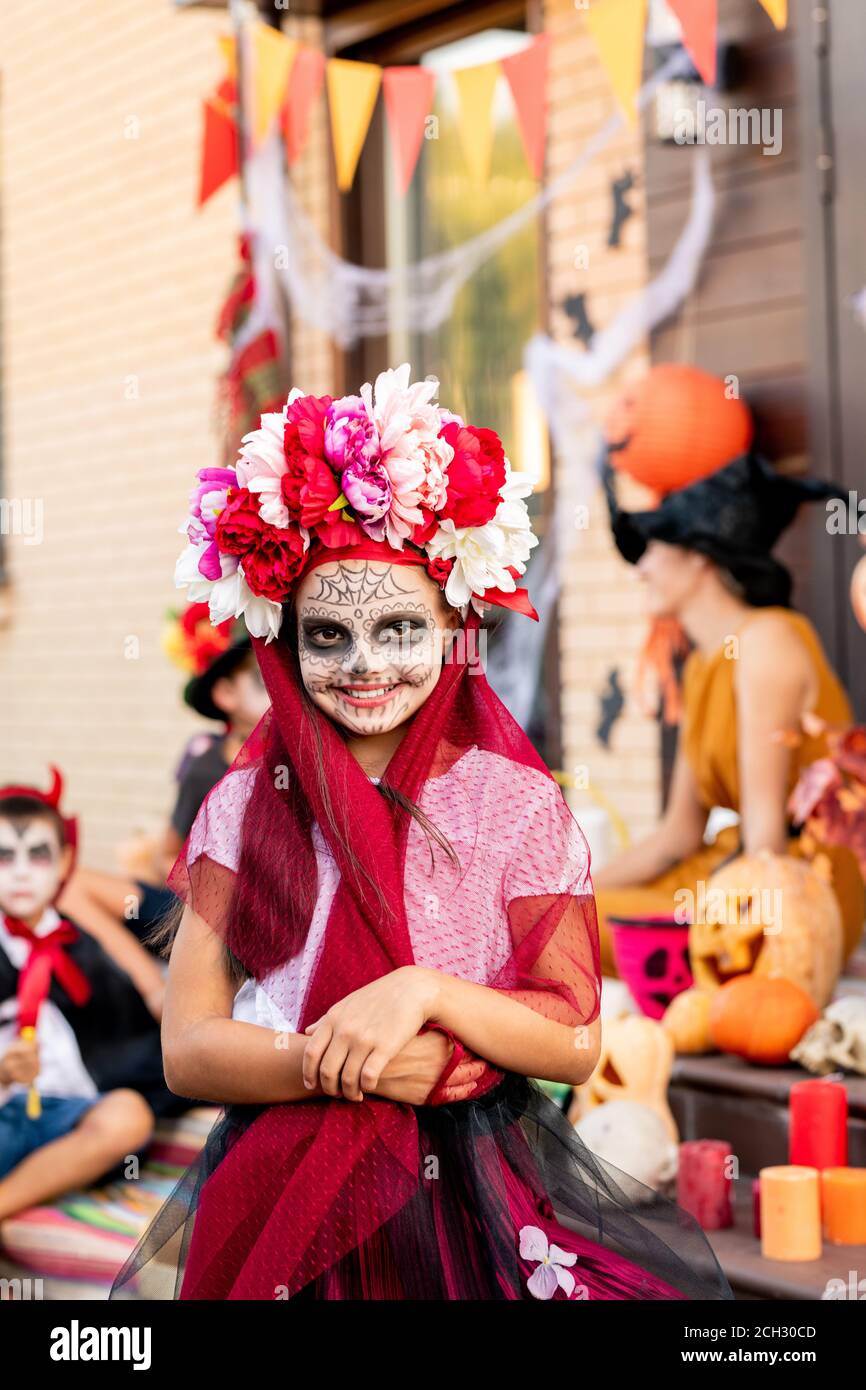 Ragazza allegra con faccia dipinta che ti guarda con sorriso contro i suoi amici Foto Stock