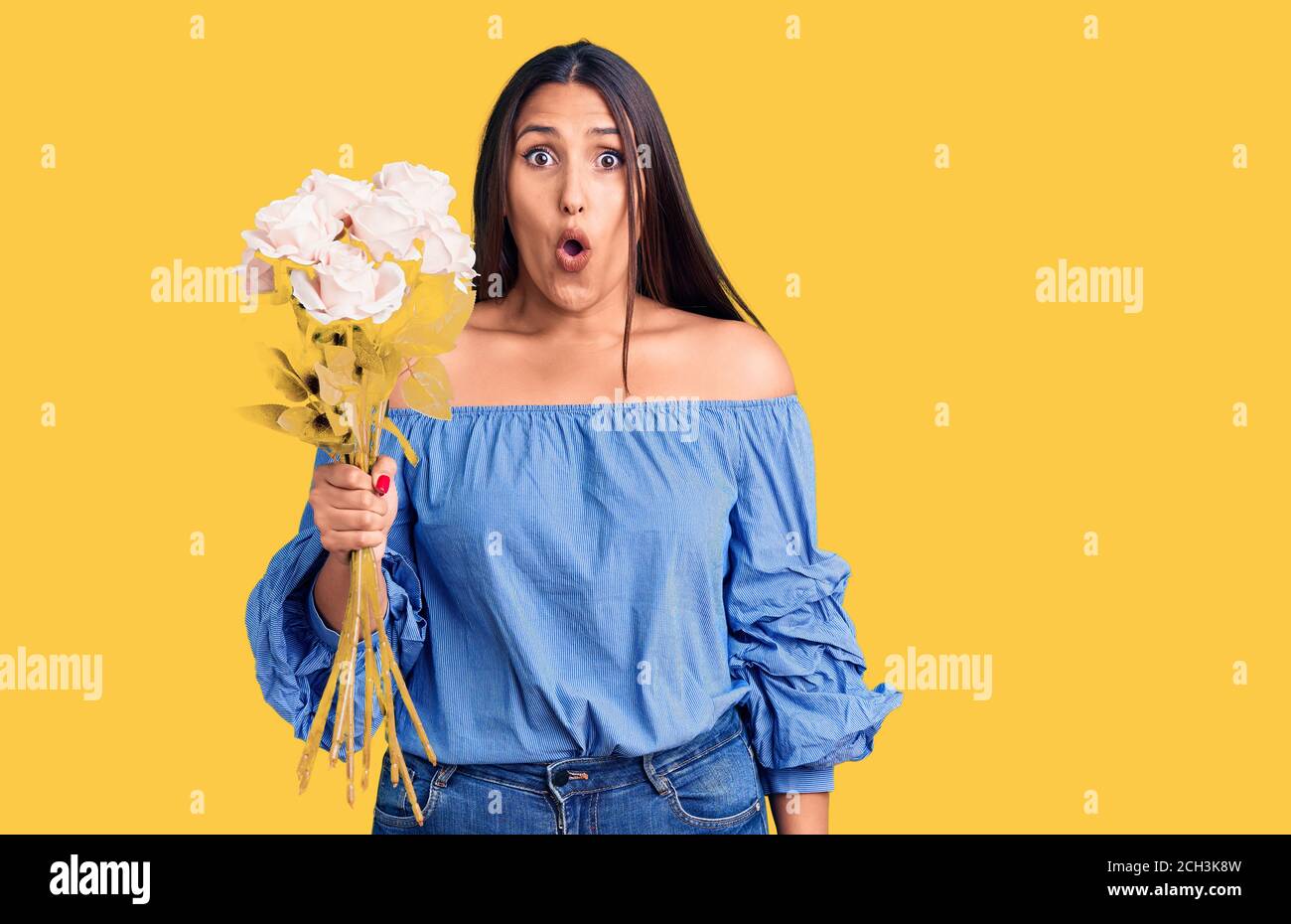 Giovane bella donna brunette che tiene bouquet spaventato e stupito con bocca aperta per sorpresa, viso incredulo Foto Stock