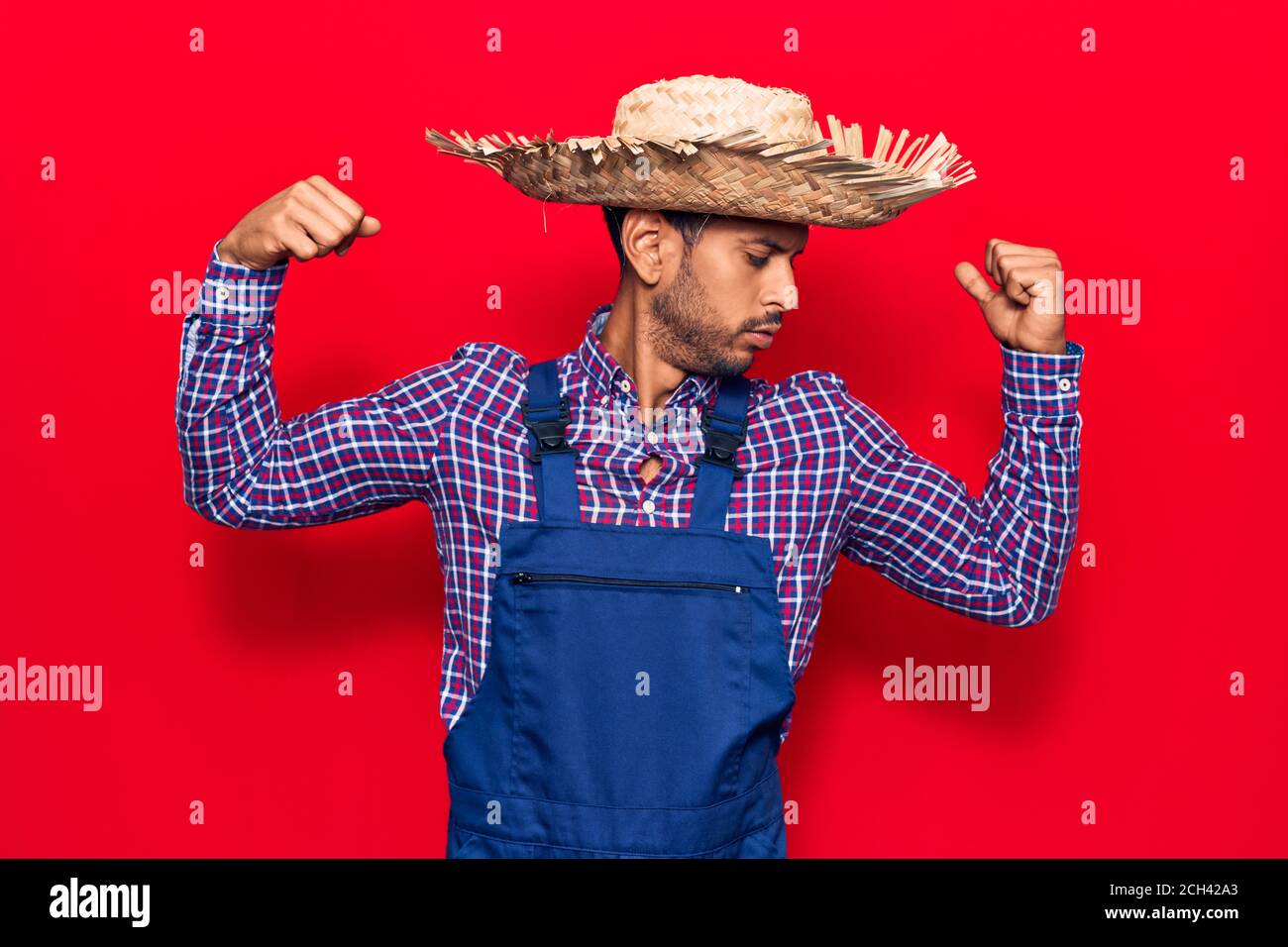 Giovane uomo latino che indossa cappello contadino e grembiule mostrando i  muscoli delle braccia sorridendo orgoglioso. Concetto di fitness Foto stock  - Alamy