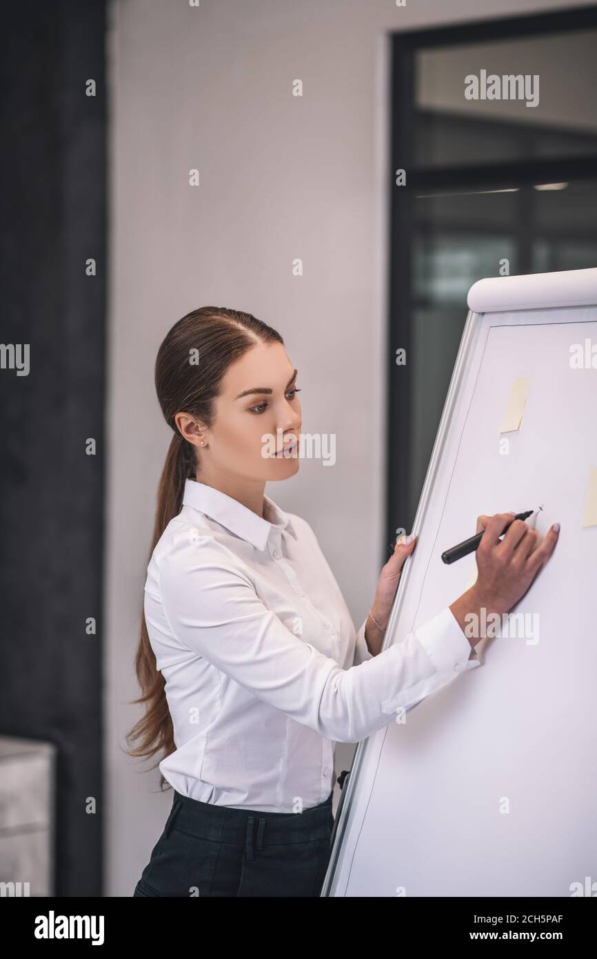 Donna con capelli castani in camicia bianca su lavagna a fogli mobili Foto Stock