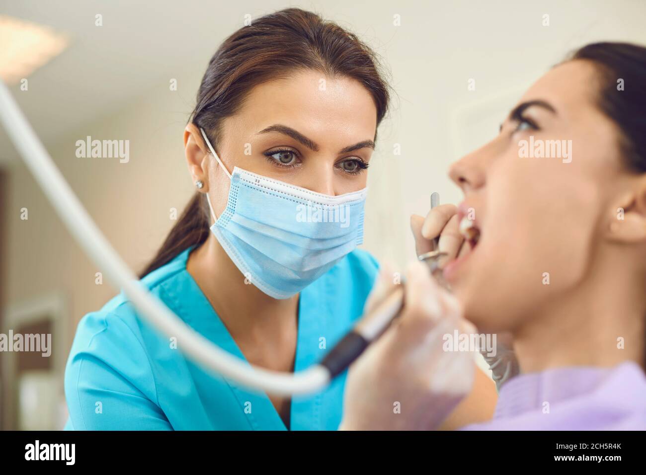 Donna medico dentista in maschera medica facendo cura professionale di dente per paziente donna in clinica dentale Foto Stock