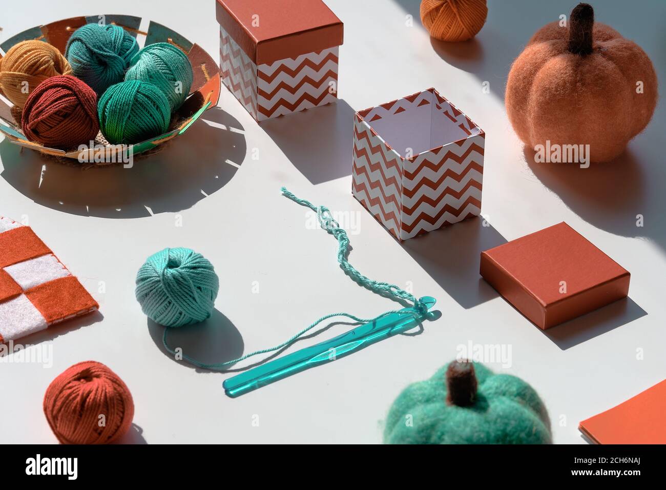 Disposizione geometrica creativa di materiali artigianali per maglieria e uncinetto con lunghe ombre. Varie palle di filato, uncino a uncinetto con filo. Decorativo Foto Stock