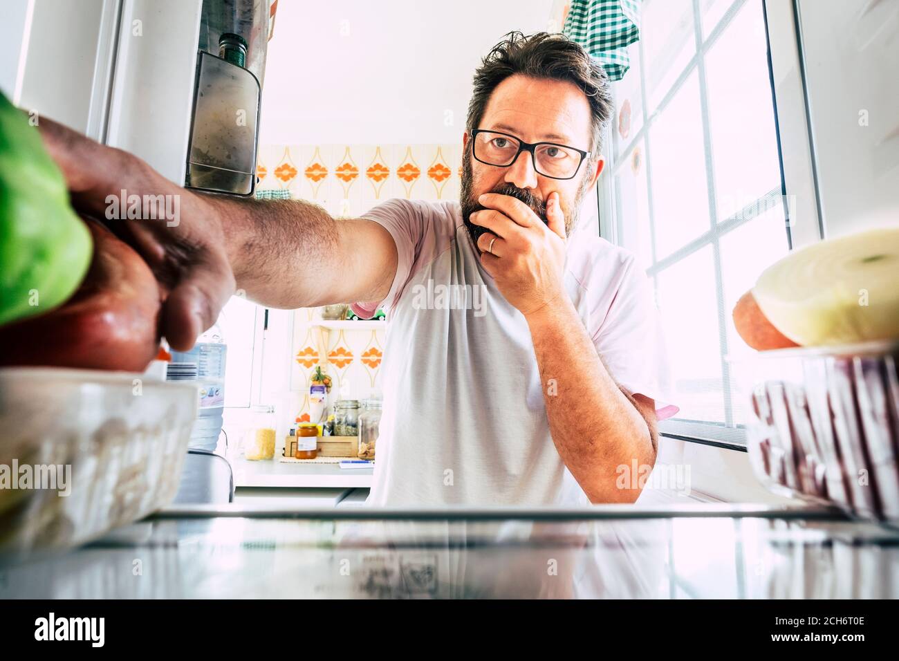 Uomo caucasico adulto che guarda all'interno del frigorifero pensando e scegliendo cosa mangiare per pranzo o cena a casa - concetto di persone e cibo per la dieta e wei Foto Stock