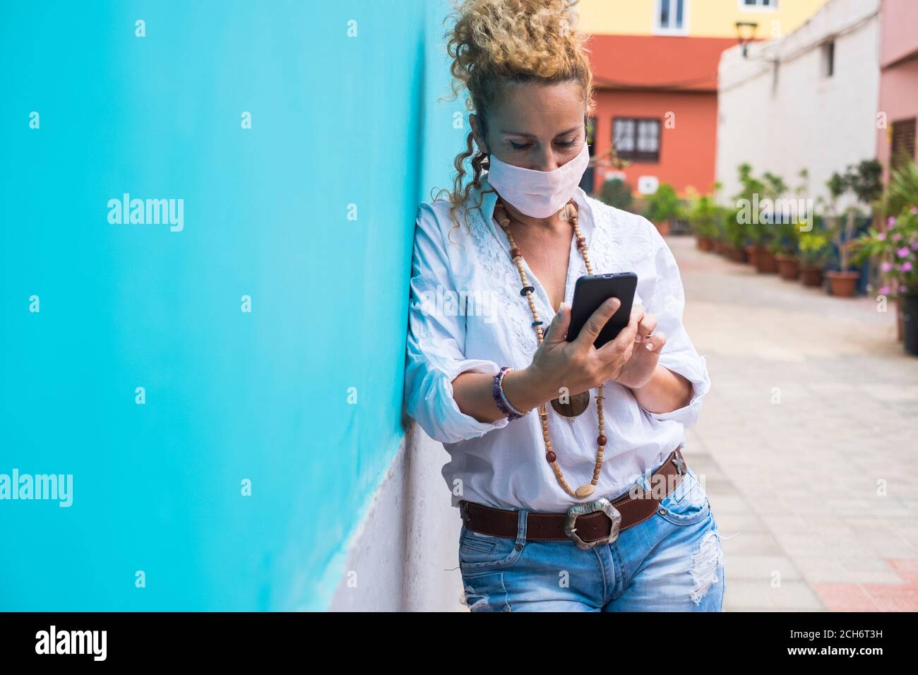 Trendy bella donna usare maschera di coronavirus protettivo in esterno dentro la strada mentre si utilizza un moderno telefono cellulare per scrivere o. Leggi - persone e nuovo normale Foto Stock