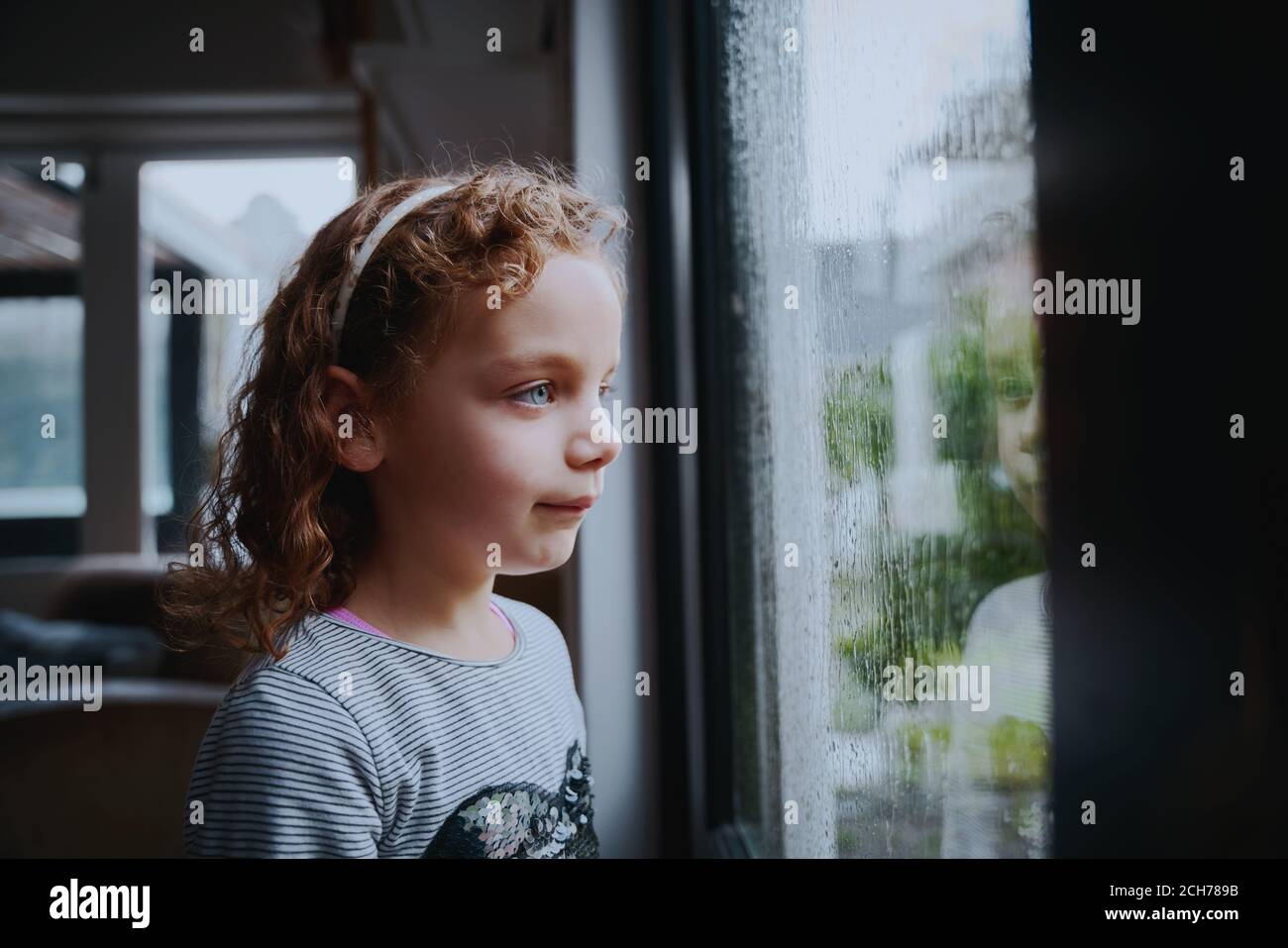 Ragazza annoiata in piedi vicino alla finestra guardando la pioggia Foto Stock