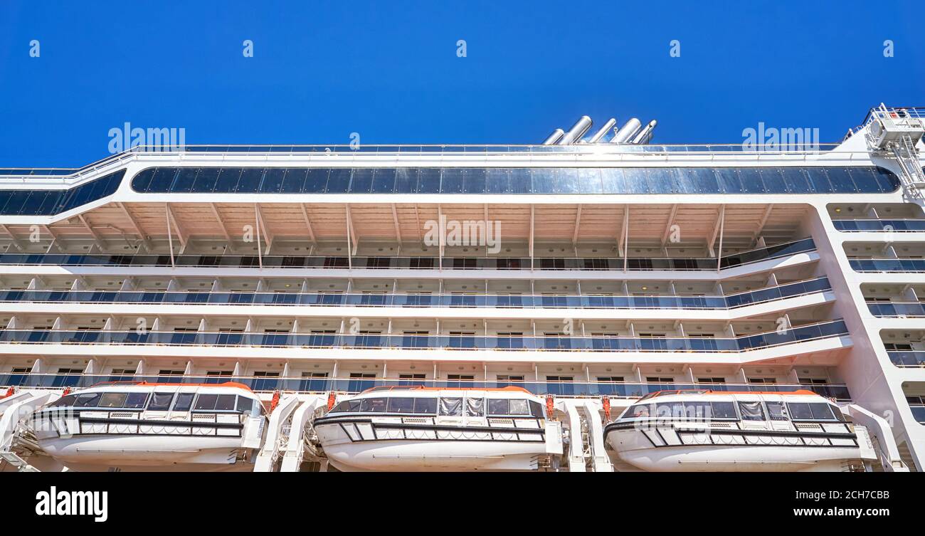 Nave da crociera con imbarcazioni di salvataggio dal lato sotto un cielo blu chiaro con sole riflettente. Foto Stock