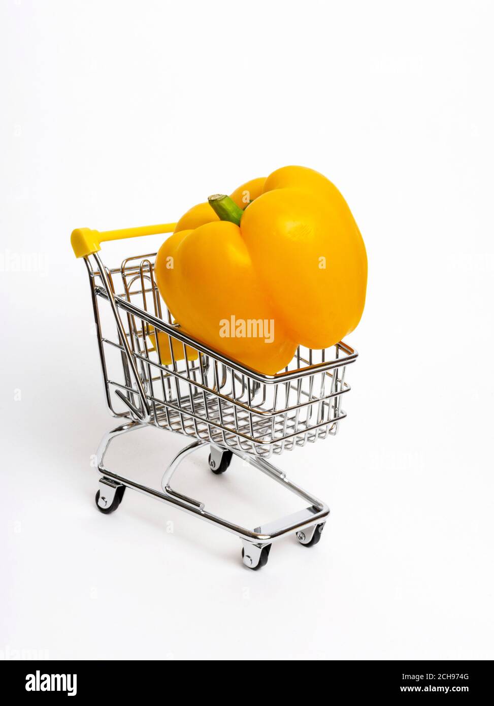 Il peperone giallo brillante poggia su un piccolo carrello su un semplice sfondo bianco Foto Stock