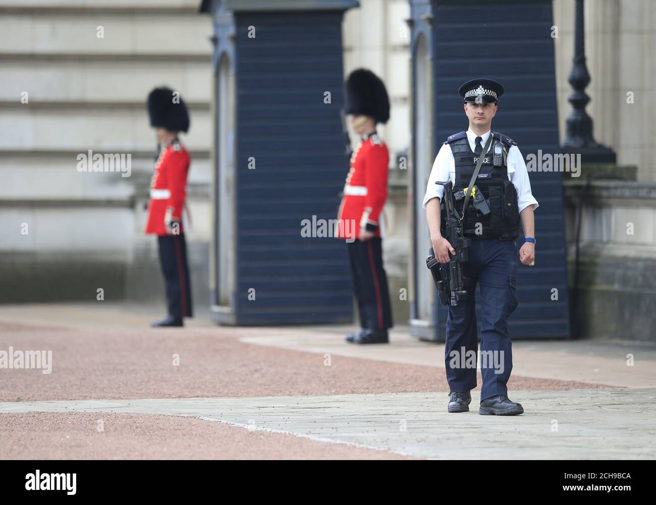 Un ufficiale di polizia armato e soldati delle guardie irlandesi nel piazzale di Buckingham Palace nel centro di Londra. Scotland Yard ha detto che un uomo di 41 anni è stato arrestato dopo aver scalato un muro perimetrale al palazzo mercoledì sera. Foto Stock