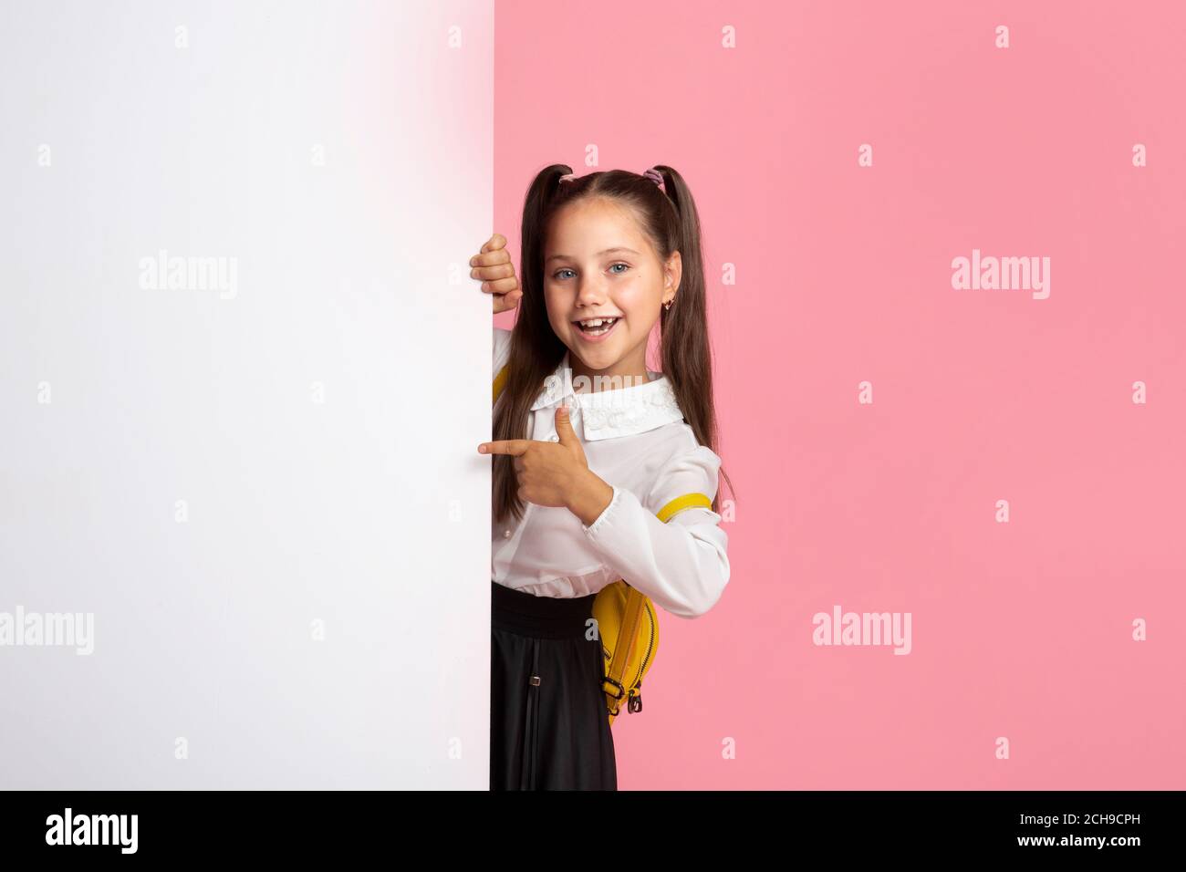 Bambina in uniforme scuola sale da cartellone con spazio vuoto e punta il dito su di esso Foto Stock