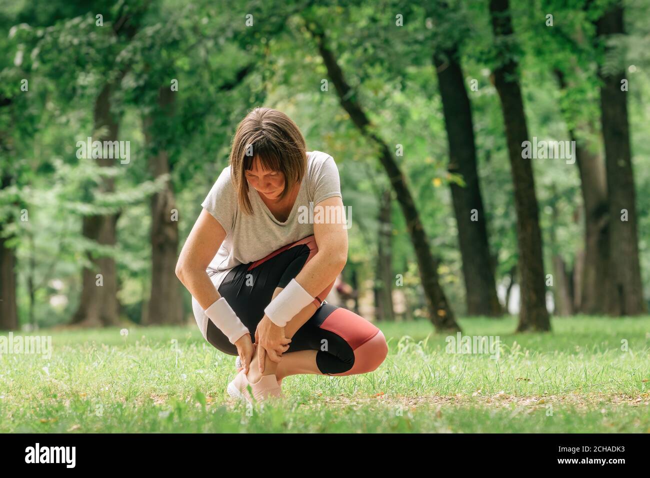 Jogger femminile con lesioni dolorose alla caviglia durante l'attività di jogging del parco, fuoco selettivo Foto Stock