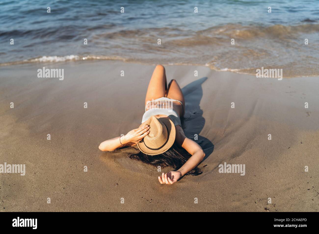 Tan ragazza in costume da bagno sdraiata sulla spiaggia vicino al mare con  cappello sul viso Foto stock - Alamy