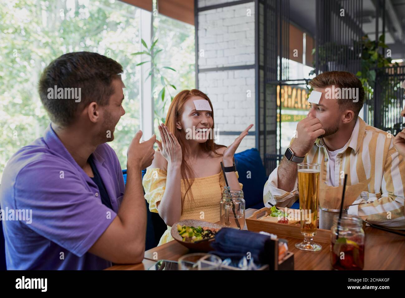 piccolo adesivo sulla fronte. amici che si divertono nel ristorante, caucasici giovani che giocano un hedbanz gioco, ridere Foto Stock