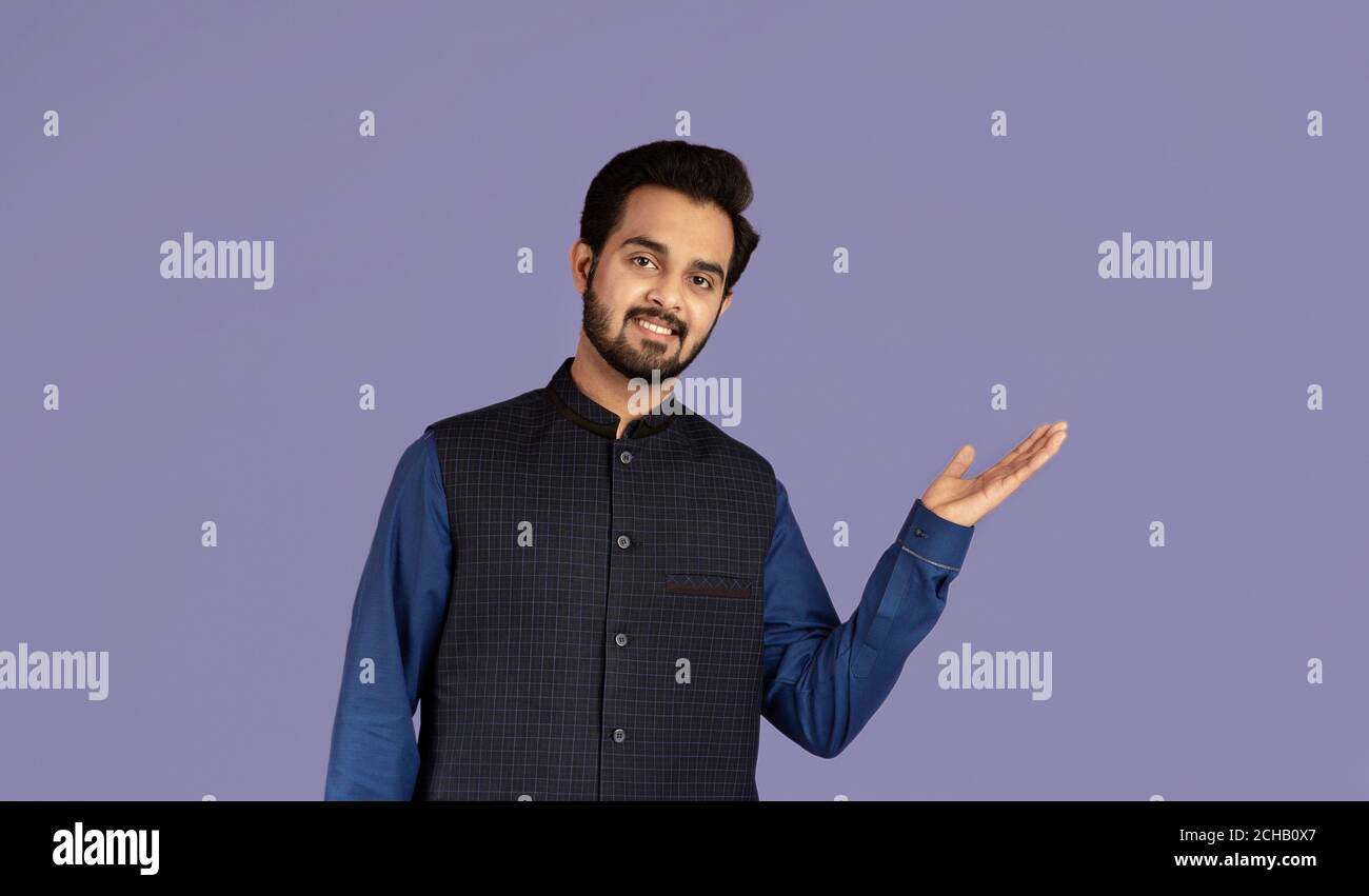 Allegro uomo indiano che presenta qualcosa su sfondo viola, spazio per il vostro prodotto design Foto Stock