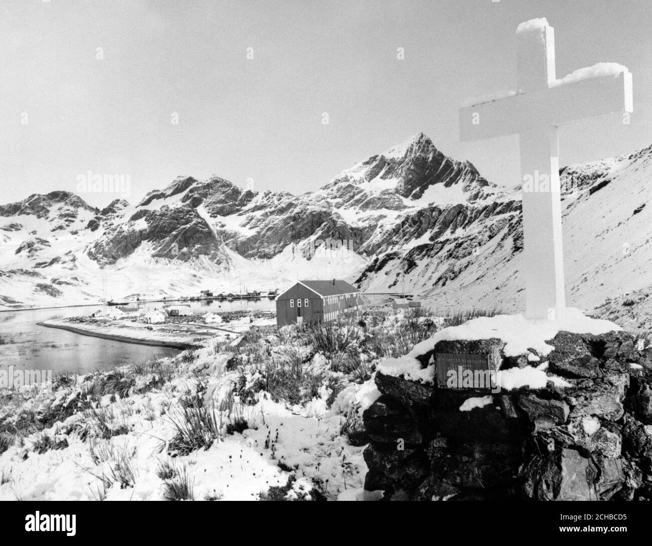 La Memorial Cross a Sir Ernest Shackleton a Hope Point, Georgia del Sud, si affaccia sulla stazione Grytviken (il grande edificio a tre piani) del British Antartic Survey e sui vecchi edifici governativi. Shackleton subì un attacco di cuore e morì a bordo della sua nave la 'quest' mentre fu ancorata a Grytviken il 5 gennaio 1922. Fu sepolto nel cimitero di Grytviken. Foto Stock