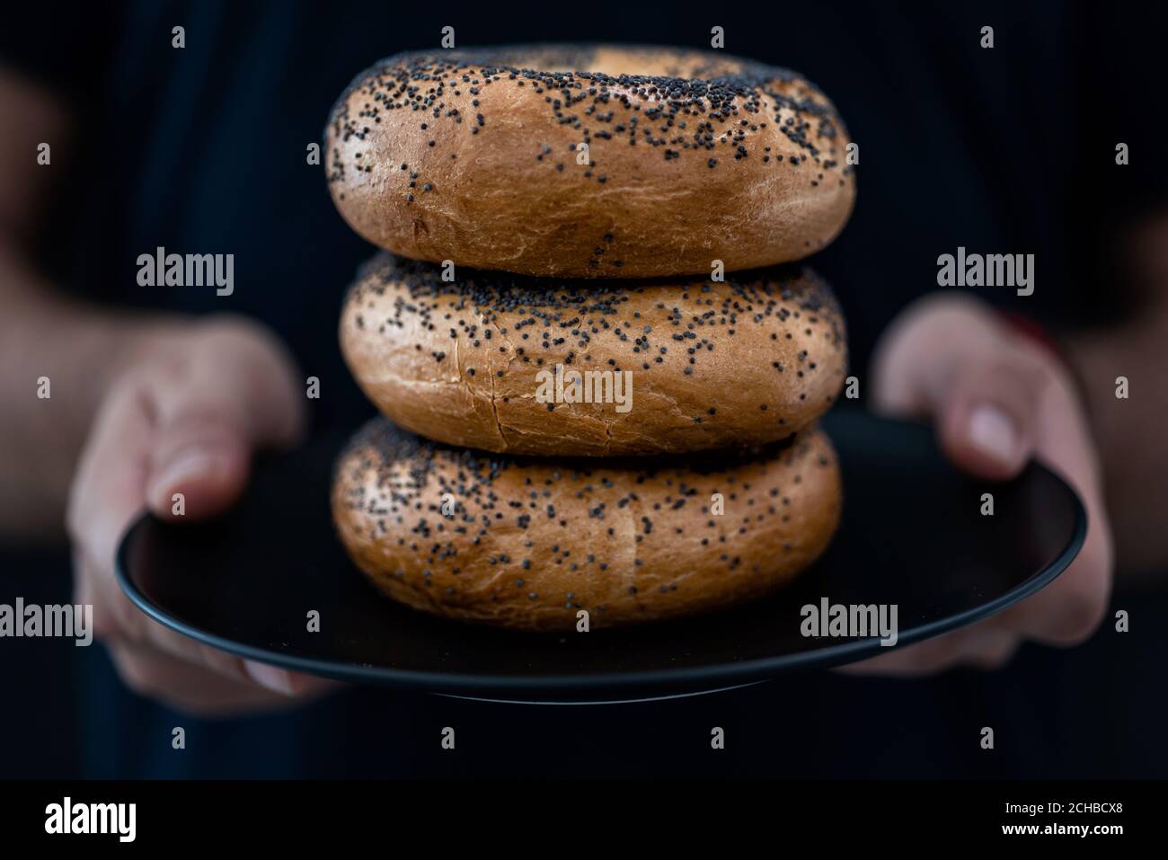 Le mani degli uomini tengono un piatto pieno di bagel Uno sfondo nero Foto Stock