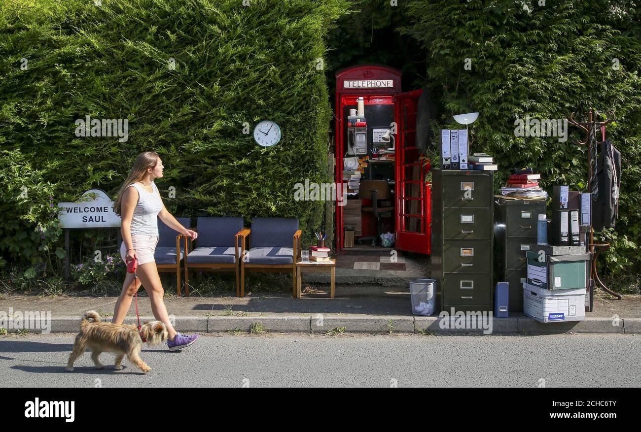 Residente nel villaggio, Sophie Pockett e il suo cane Paddy Walk passano una casella telefonica BT nel villaggio di Saul in Gloucestershire, Che è stato trasformato in ufficio britannico per Jimmy McGill, il personaggio immaginario di Better Call Saul, prima della sua prima rete su BT TV martedì 27 giugno. Foto Stock
