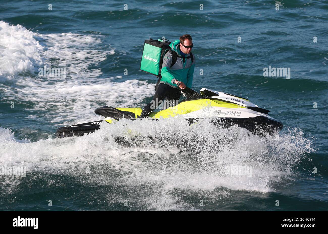 Ross Ceaton offre pasti da asporto agli amanti della spiaggia a Bournemouth via jet ski, come servizio di consegna di cibo su richiesta Deliveroo sperimenta una nuovissima flotta di consegne di acqua sulla costa meridionale. Foto Stock