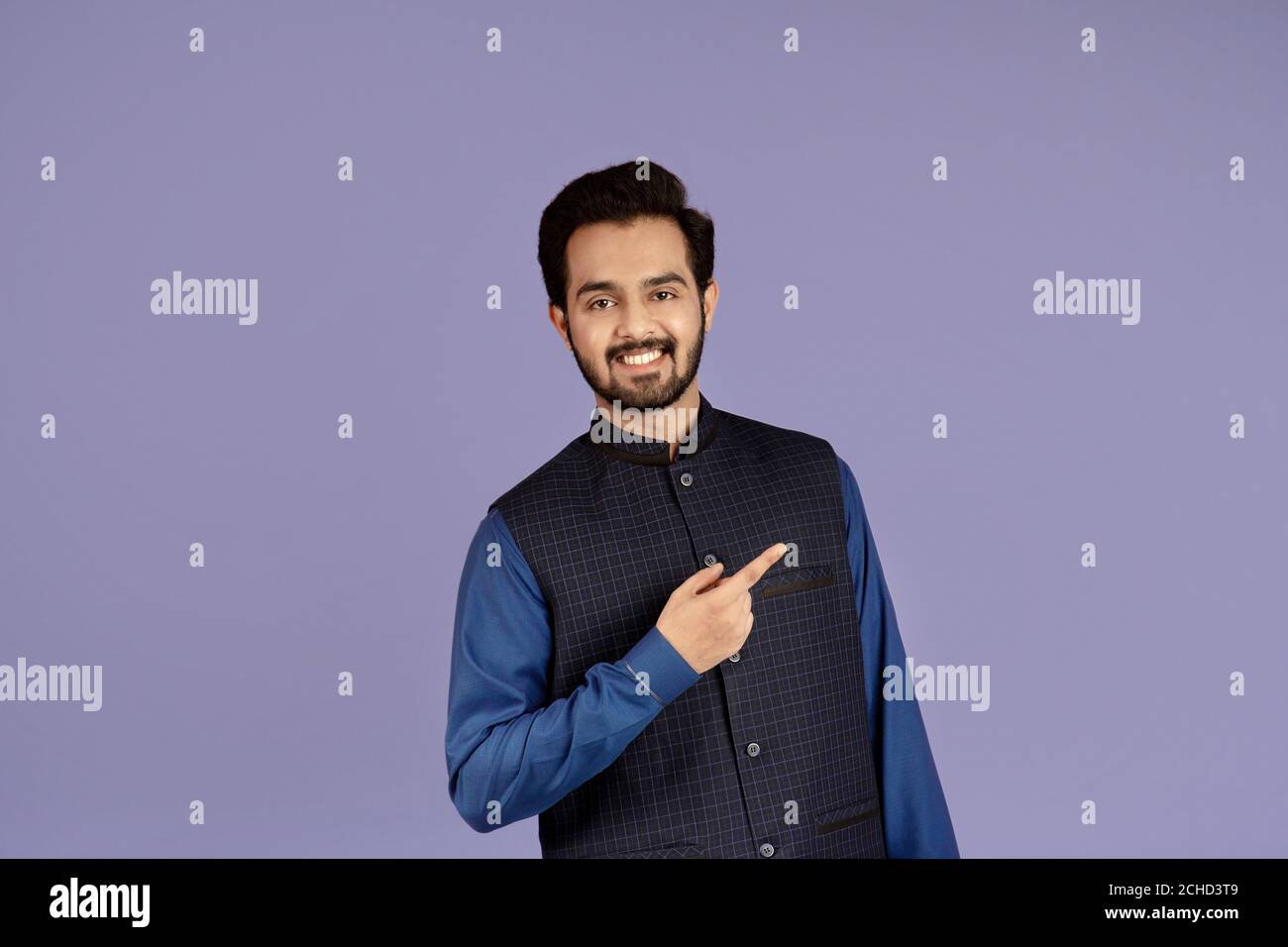 Bel giovane indiano sorridente e che punta da parte sul lilla sfondo Foto Stock